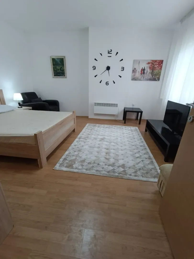 Furnished bedroom with a double bed, TV, and decorative wall clock.