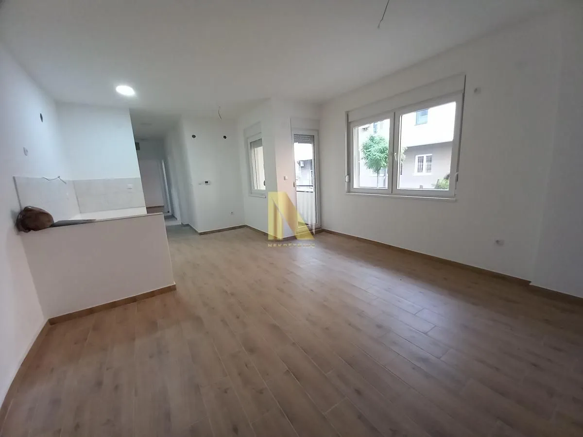 Prazna dnevna soba sa laminatom i belim zidovima.