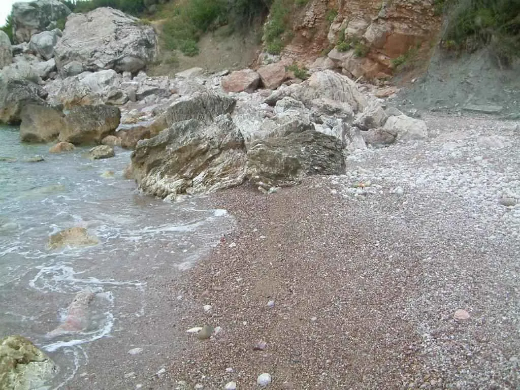 Pogled na prirodnu stjenovitu obalu i šljunkovitu plažu pored mora.