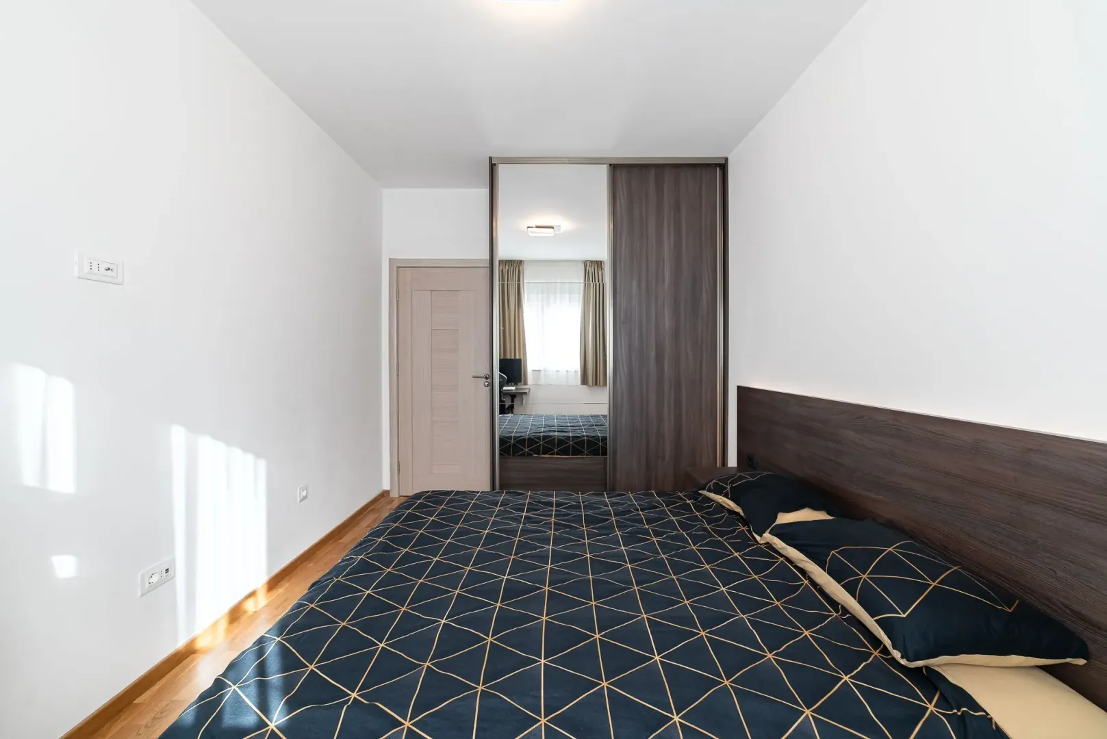 Moderna spavaća soba sa bračnim krevetom i ugradnim plakarom sa ogledalom.