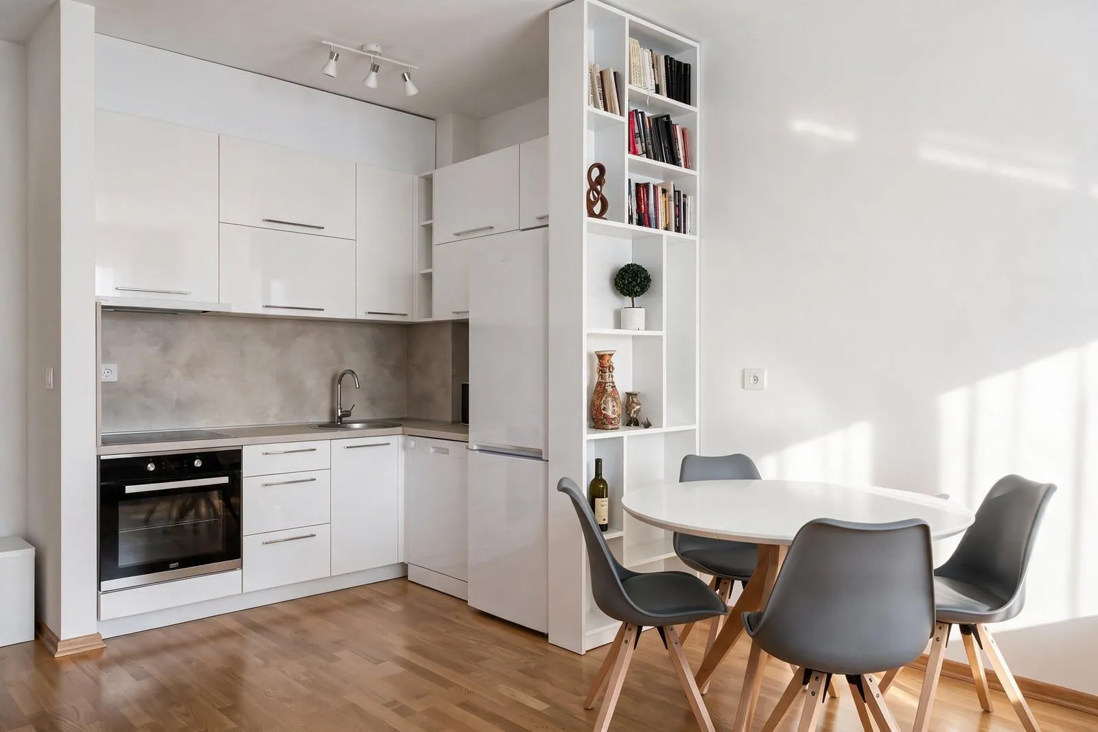 Modern white kitchen with a dining area and built-in shelving.
