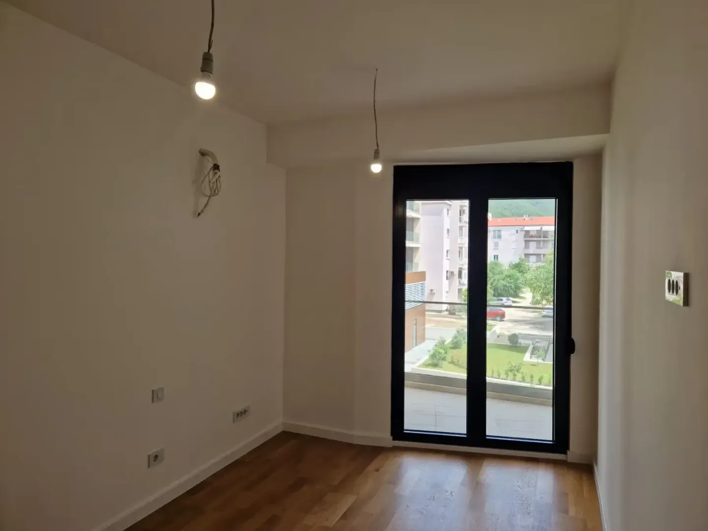 Prazna soba sa drvenim podom i izlazom na terasu.