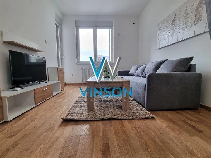 Dnevna soba sa garniturom, televizorom i drvenim podom.