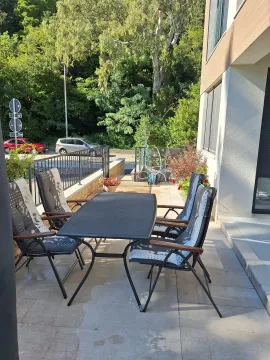 Terasa sa trpezarijskim stolom i stolicama ispred ulaza u zgradu. - image 2