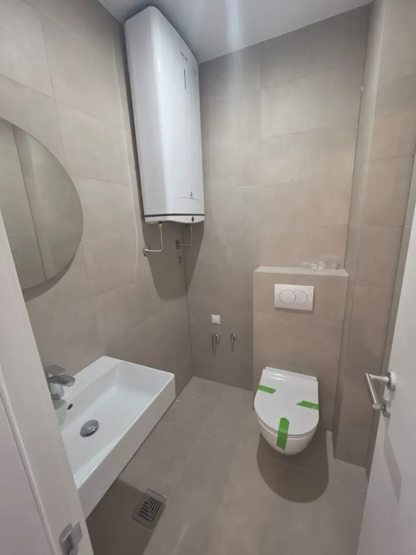 Manje kupatilo sa pločicama u neutralnim tonovima, umivaonikom i wc šoljom.