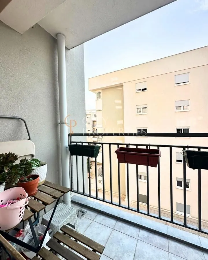 Manji natkriveni balkon sa drvenim stolom i pogledom na susjedne zgrade.