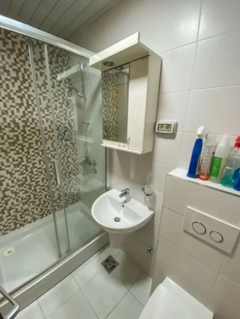 Manje kupatilo sa tuš kabinom, umivaonikom i ormarićem sa ogledalom.