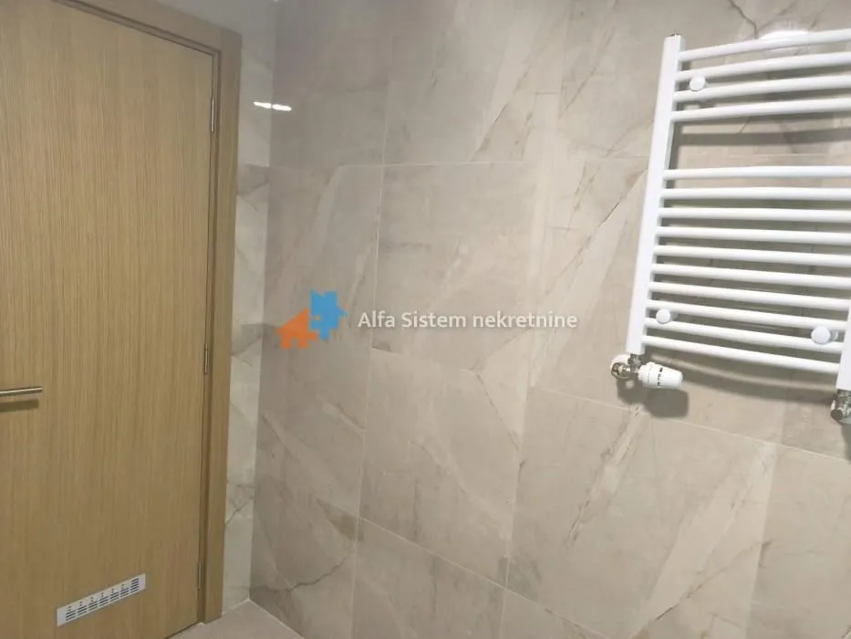 View of a section of the bathroom with beige tiles, a wooden door, and a white radiator.