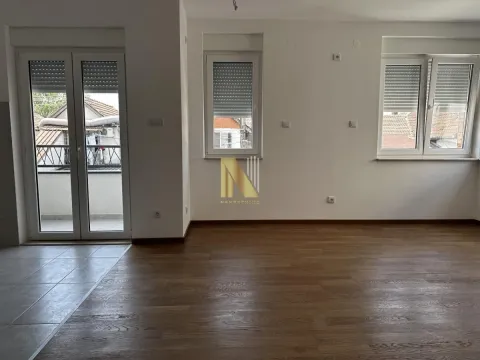 Prazna dnevna soba sa drvenim podom, belim zidovima i izlazom na terasu. - image 2