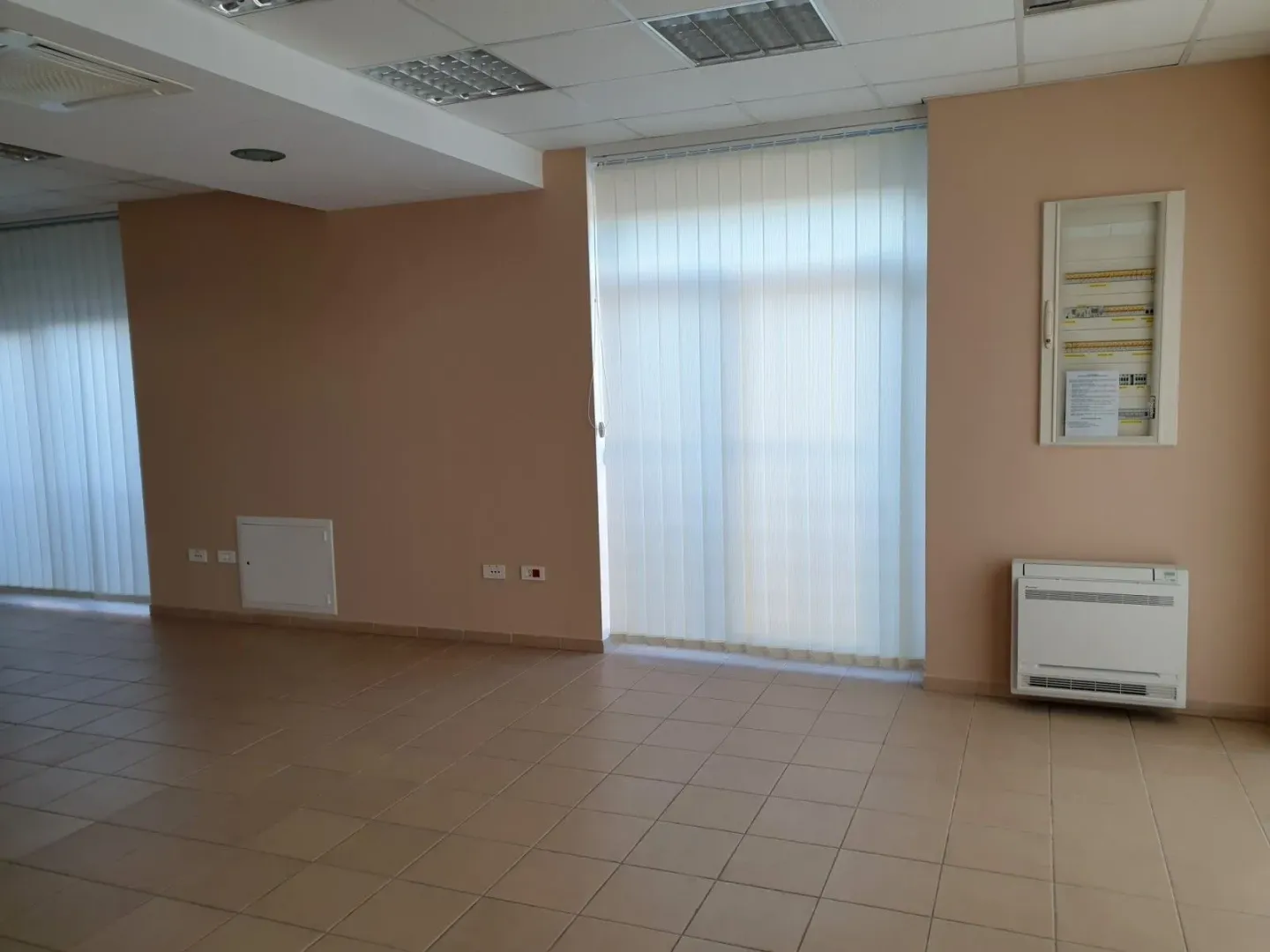 A spacious empty room with tiled flooring and vertical blinds.