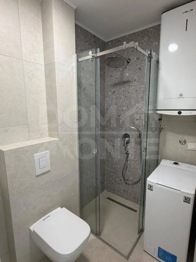 Modern bathroom with a shower cabin, toilet, and washing machine.