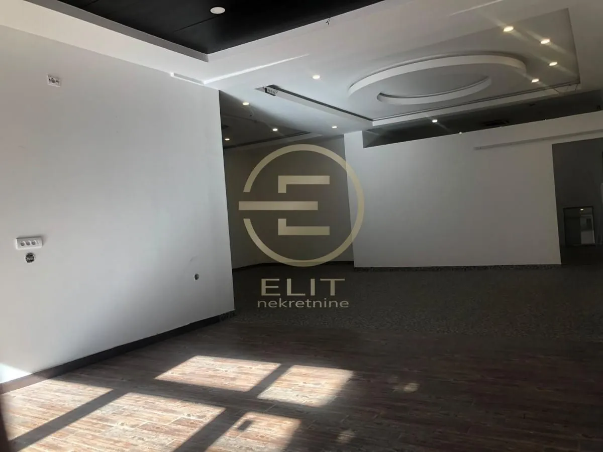Empty spacious room with dropped ceiling and wooden flooring.