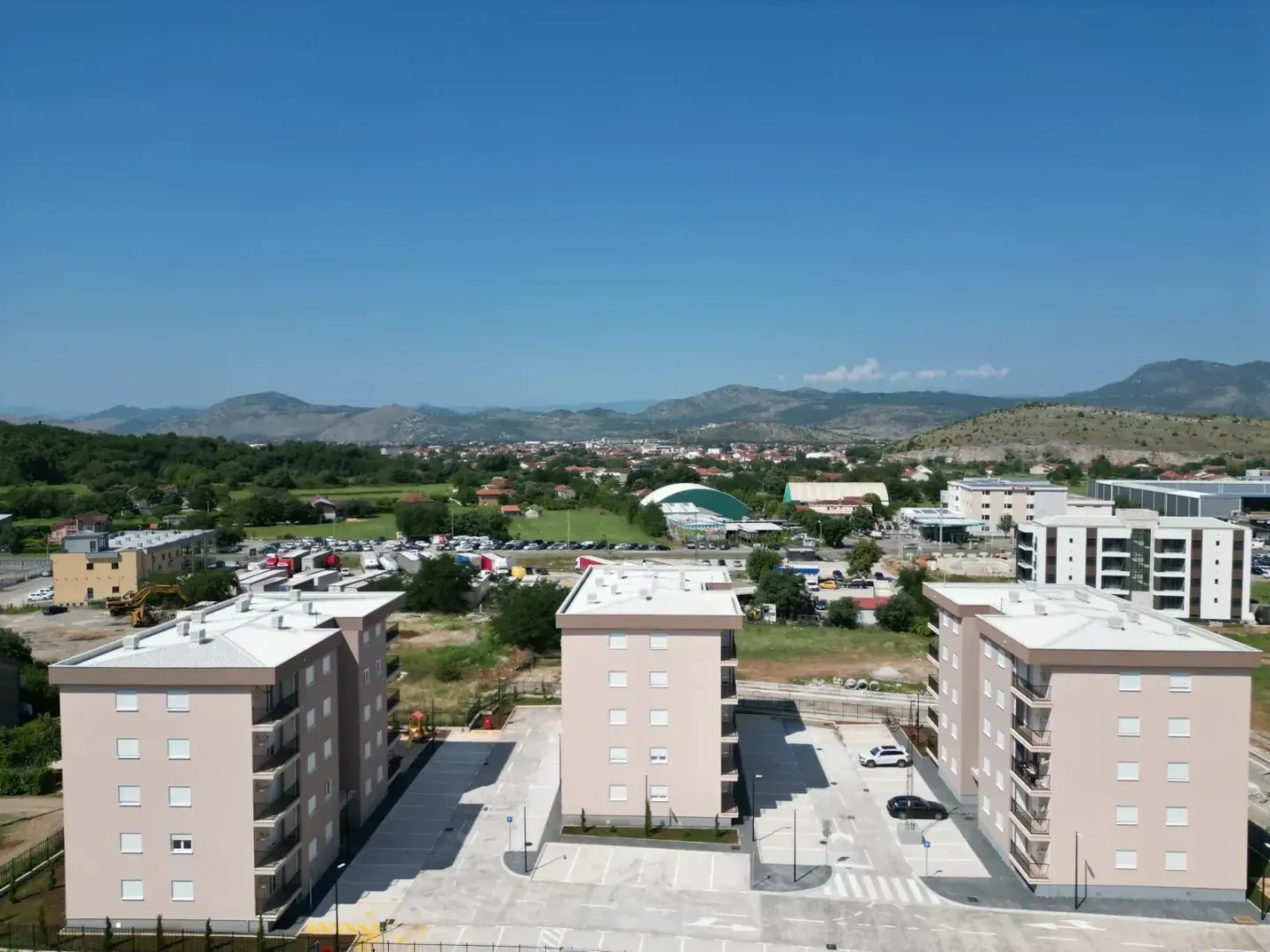 Pogled iz vazduha na stambene zgrade i okolno naselje sa brdima u pozadini.