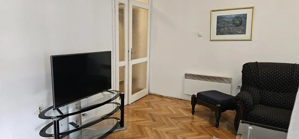 Dnevna soba sa televizorom, foteljom i parketom na podu.