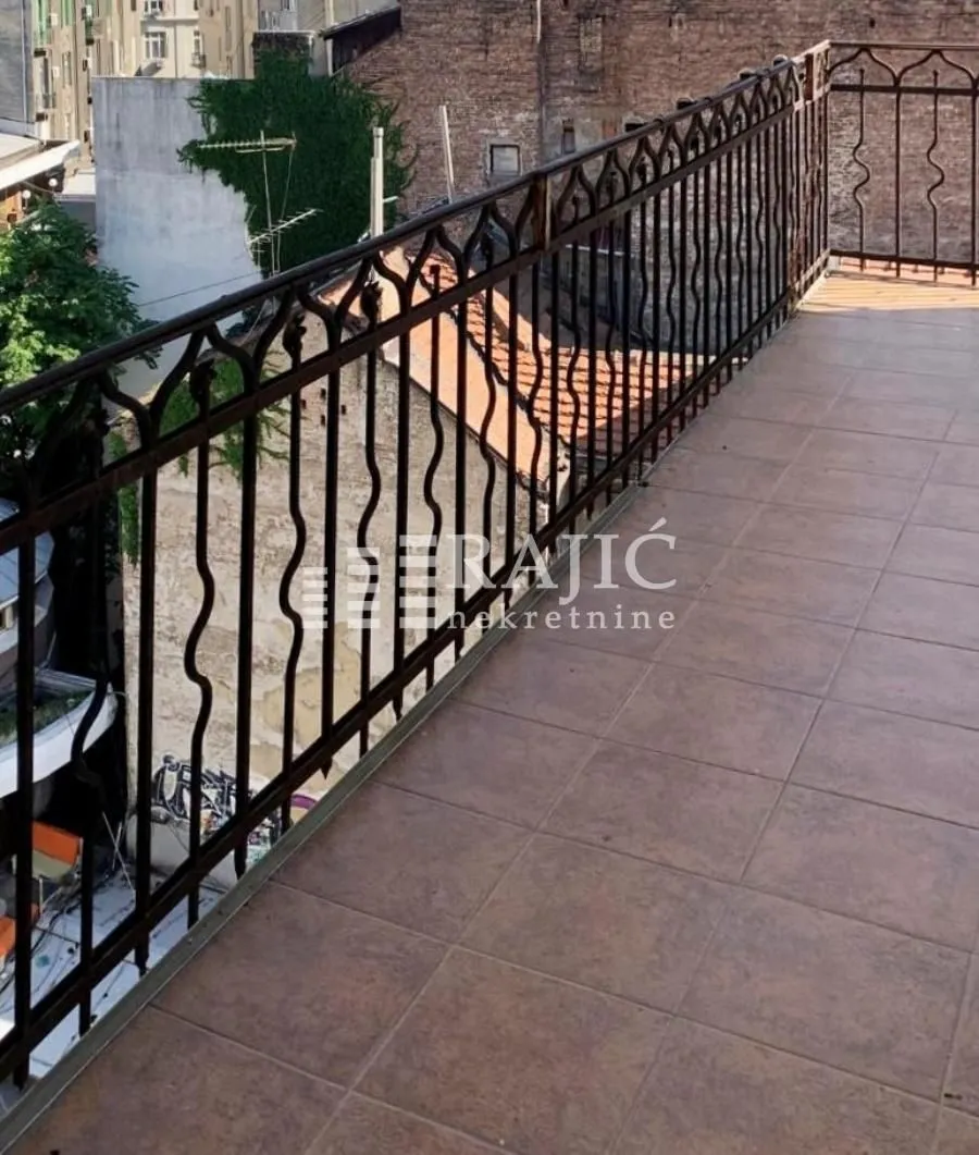 Spacious tiled terrace with metal railing and view of surrounding buildings.