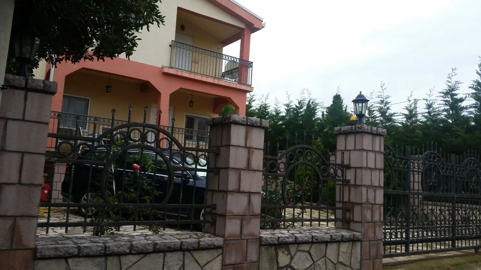 Pogled na dvorište i fasadu kuće sa ukrasnom ogradom.