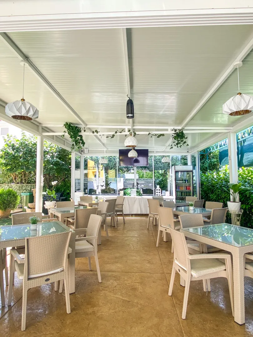 Covered and enclosed terrace furnished with tables and chairs for seating.