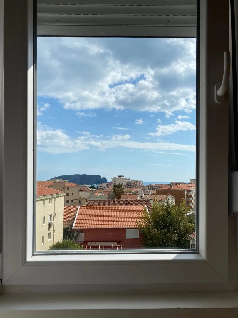 Pogled kroz prozor na naselje i more.