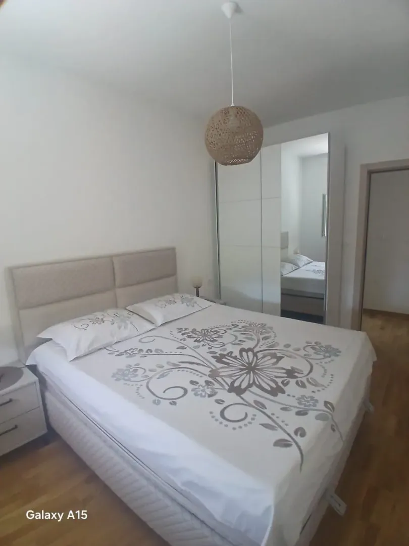 Namještena spavaća soba sa bračnim krevetom i ugradnim plakarom sa ogledalom.