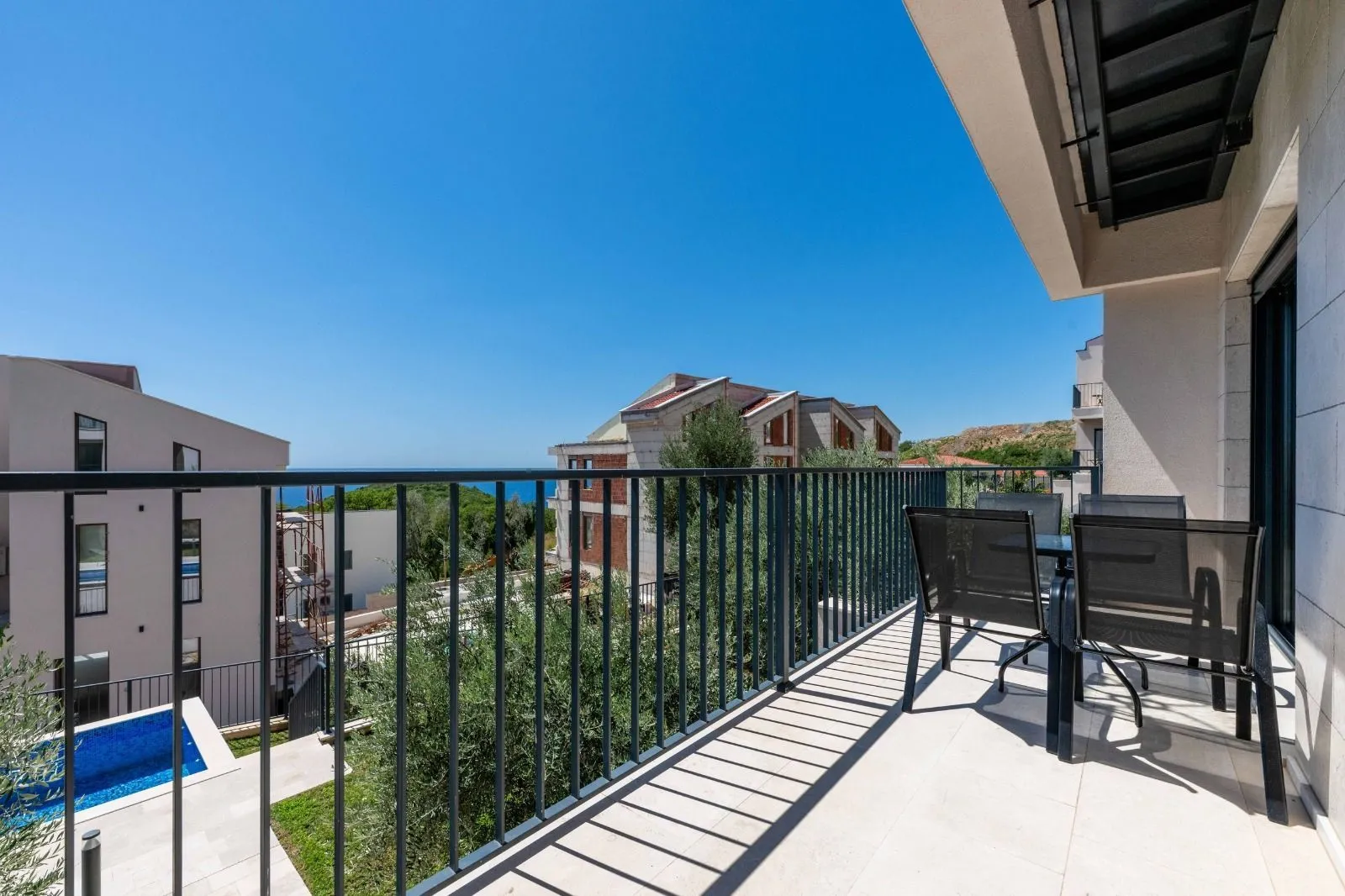 Spacious balcony with outdoor seating and a view of surrounding buildings and the sea.