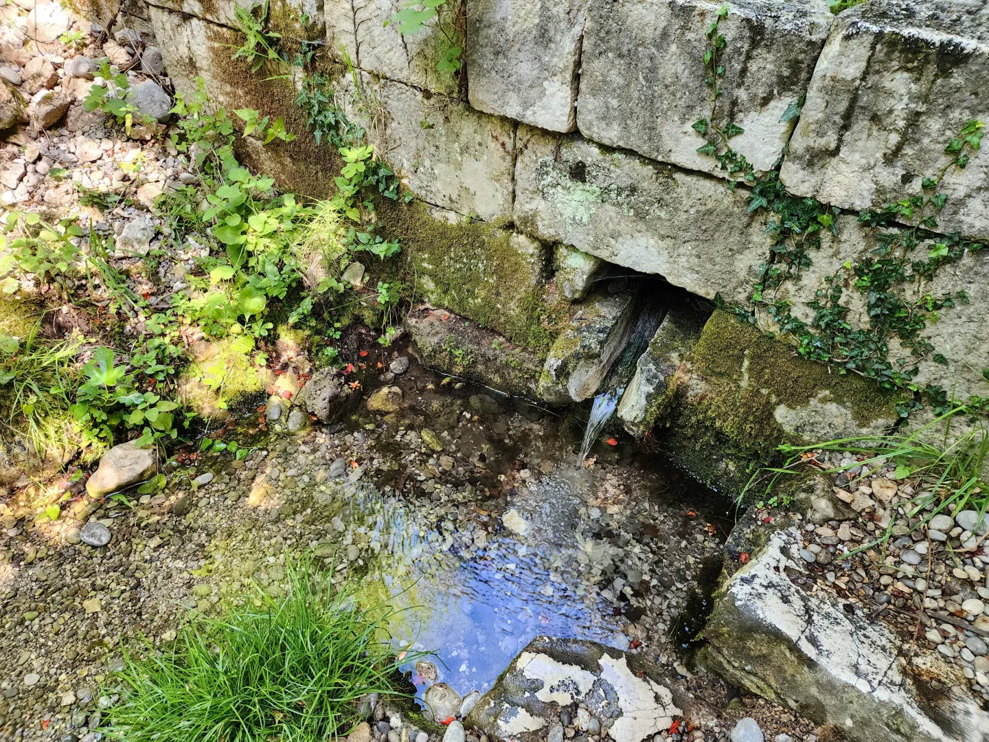 Dvorište sa kamenim zidom i malim izvorom vode.