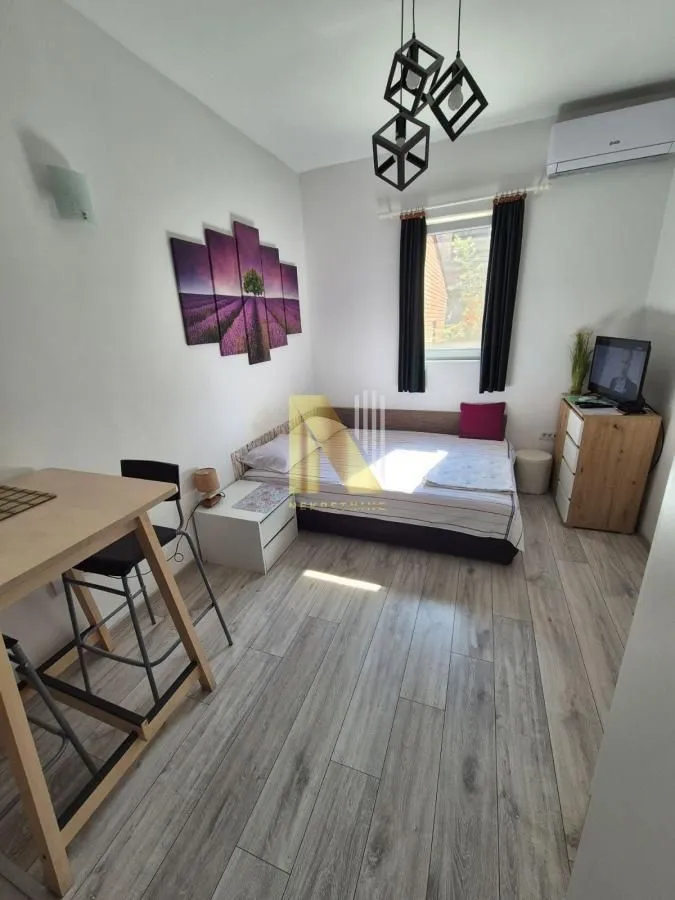 Nameštena spavaća soba sa krevetom, trpezarijskim stolom i TV komodom.
