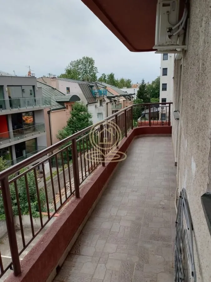 Dugačak popločani balkon sa metalnom ogradom i pogledom na naselje.