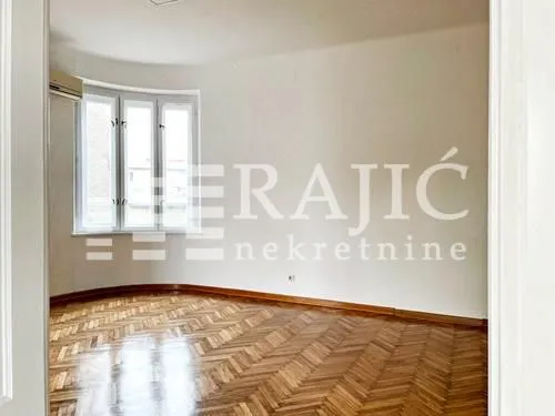 Empty room with parquet flooring and windows.