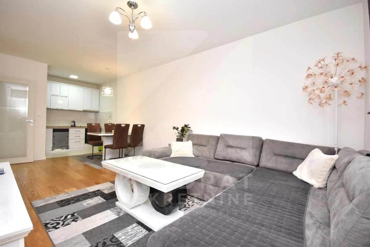 Living room with a sofa, coffee table, and a view of the kitchen and dining area.