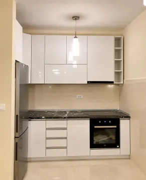 Moderna kuhinja sa bijelim elementima, tamnom radnom pločom i ugrađenim aparatima. - image 4