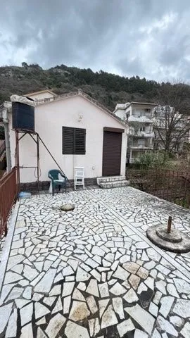 Pogled na dvorište i spoljašnjost kuće sa popločanom terasom.