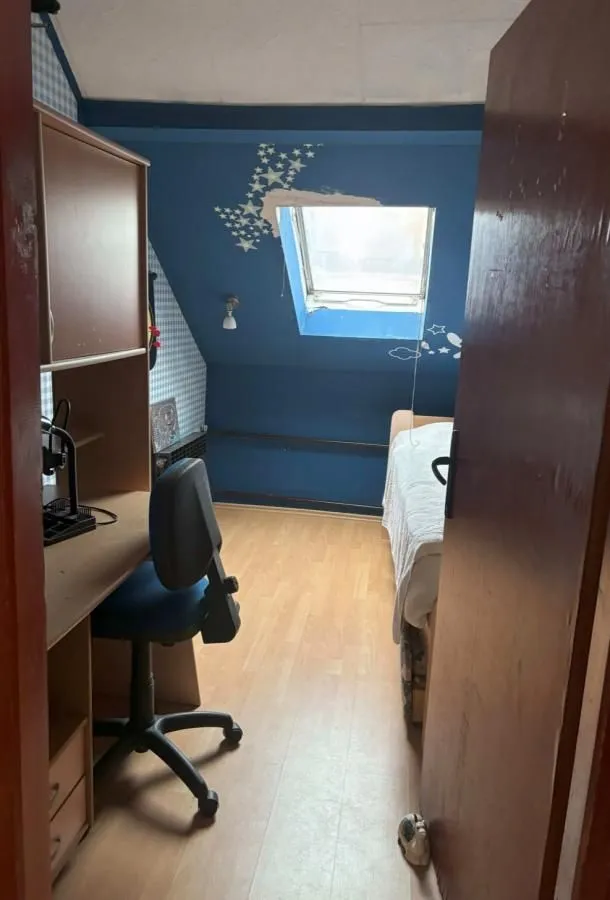 Manja spavaća soba sa krevetom, pisaćim stolom i krovnim prozorom.
