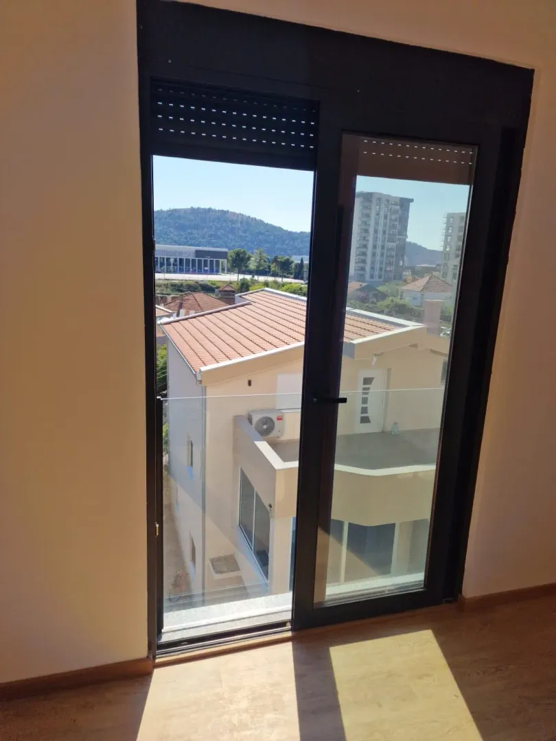 View through balcony doors towards surrounding buildings and a hill.