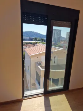 View through balcony doors towards surrounding buildings and a hill. - image 12