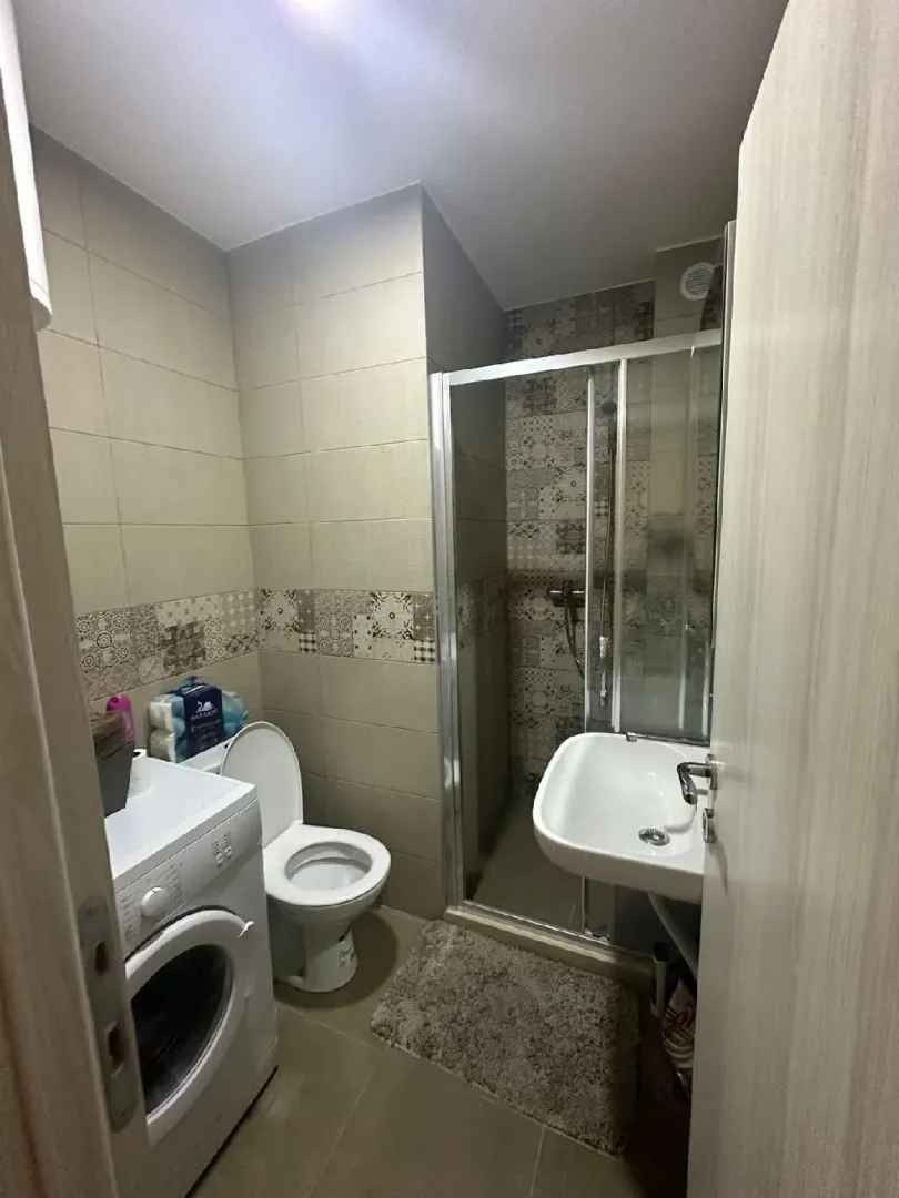 Small bathroom with a shower cabin, sink, toilet, and washing machine.