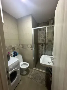 Small bathroom with a shower cabin, sink, toilet, and washing machine. - image 7