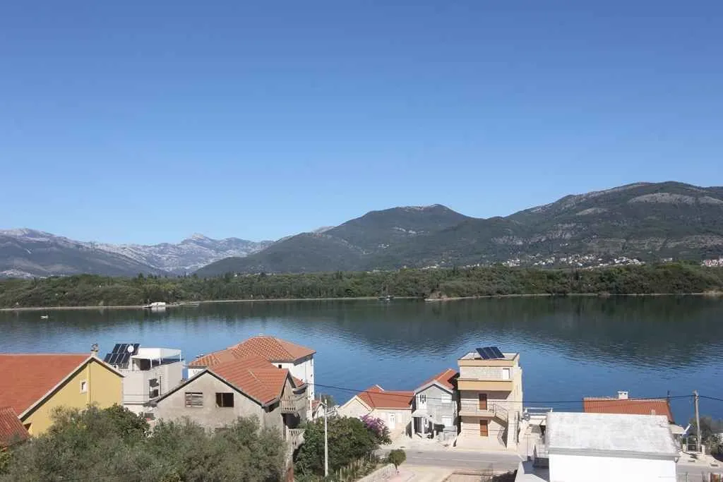 Pogled sa terase na more, kuće i planine u daljini.