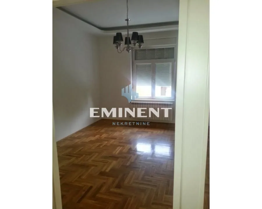 An empty room with parquet flooring and a chandelier with a view through the window.