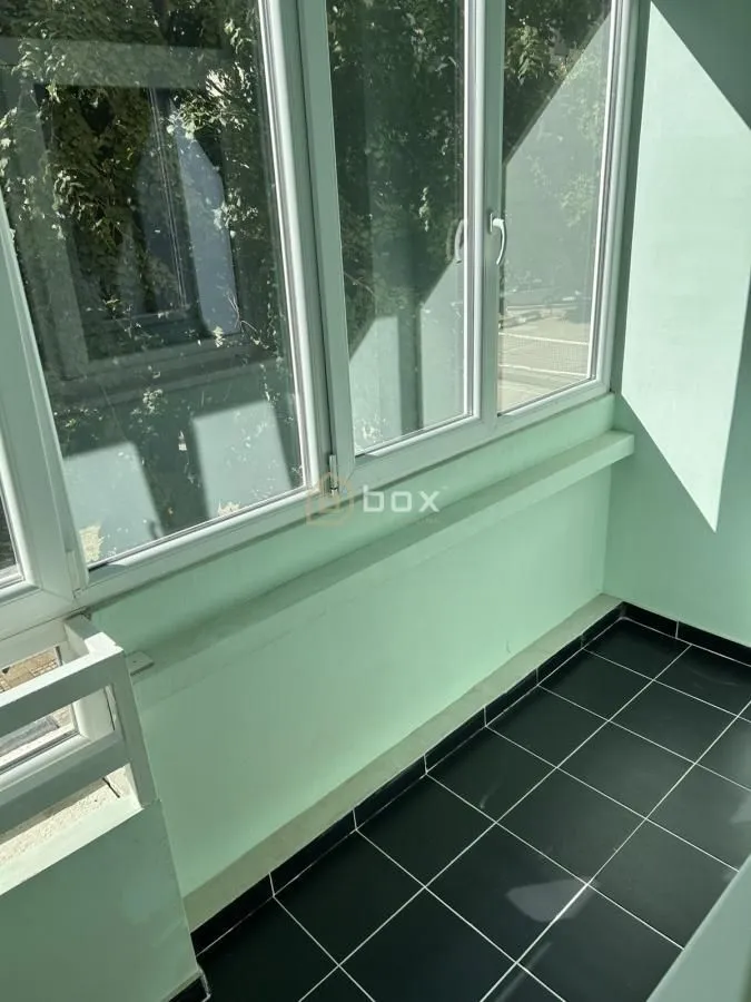 Zastakljeni balkon sa velikim prozorima i tamnim podnim pločicama.