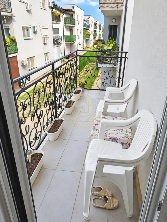 Nenatkriveni balkon sa metalnom ogradom i pogledom na dvorište zgrade.