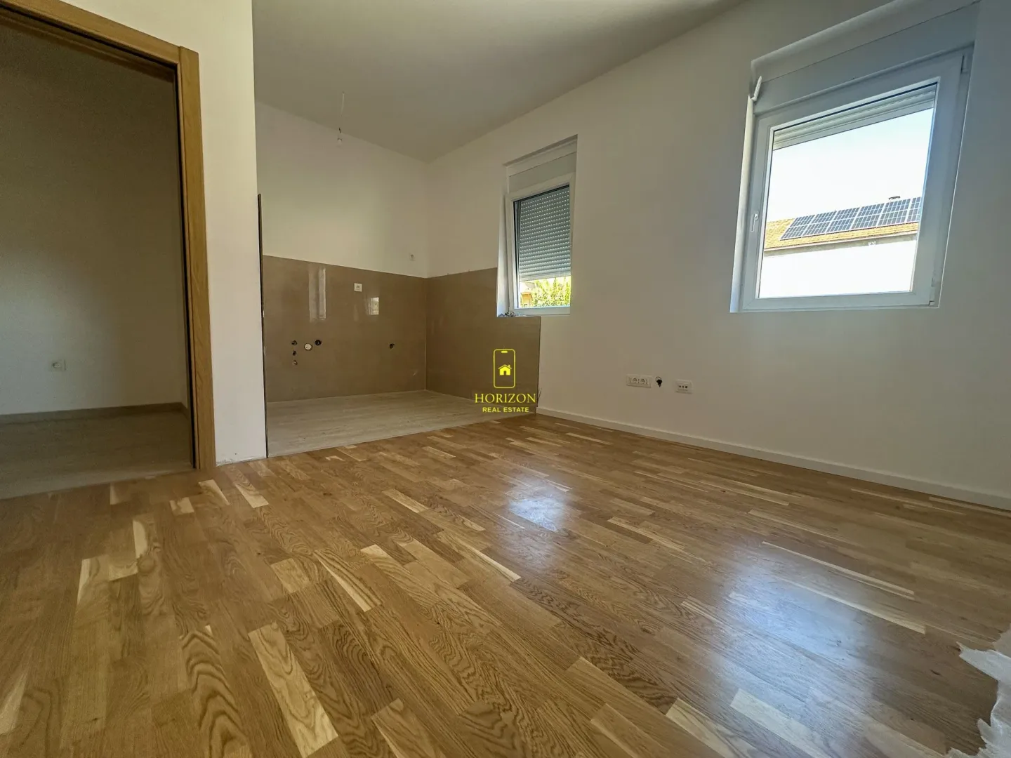 Prazna soba sa parketom i pripremljenim dijelom za kuhinju.