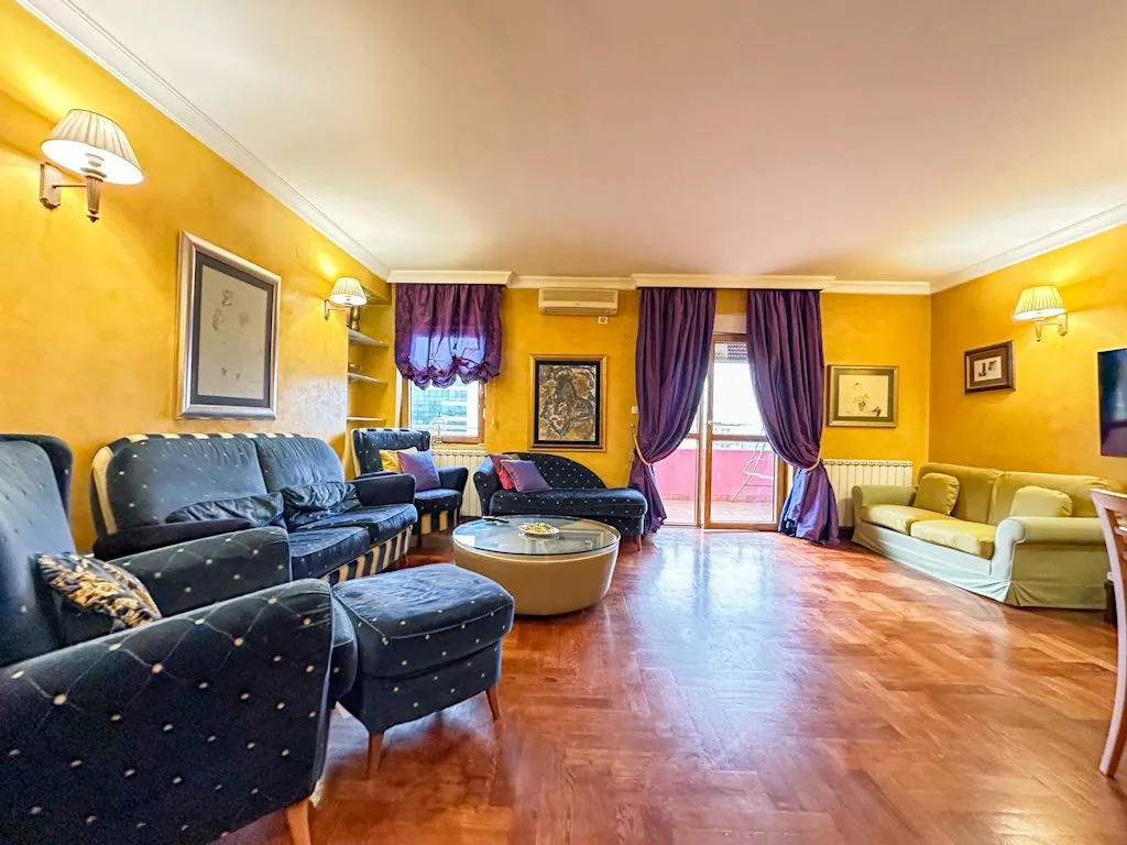 Spacious living room with seating furniture and parquet flooring.