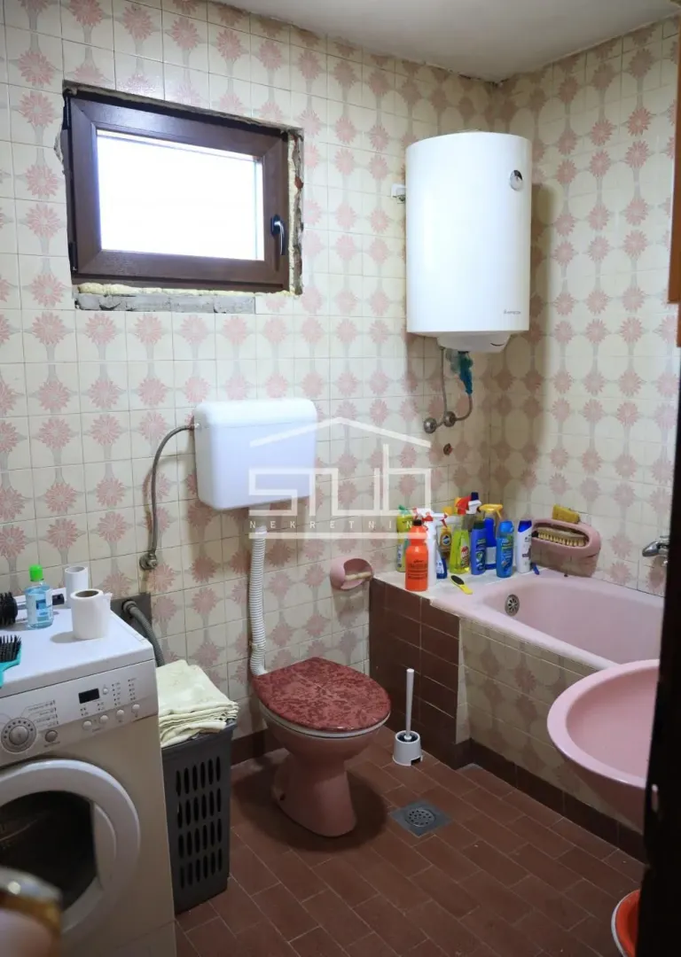 Older furnished bathroom with a bathtub, toilet, sink, and washing machine.