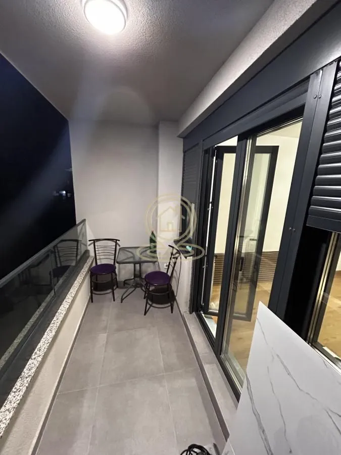 Covered balcony with seating furniture and a glass railing.