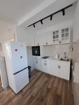 Manja bijela kuhinja sa bijelim frižiderom i drvenim podom. - image 6