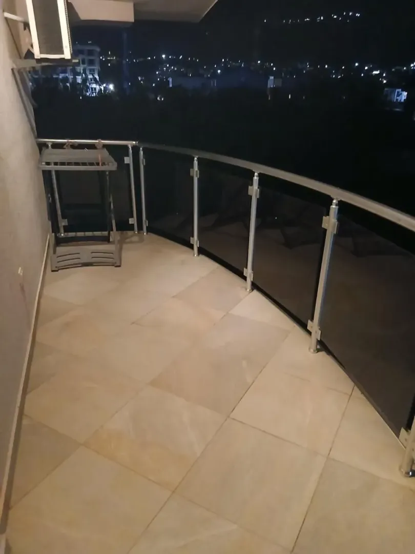 Prostrana popločana terasa sa metalnom ogradom i pogledom na grad noću.