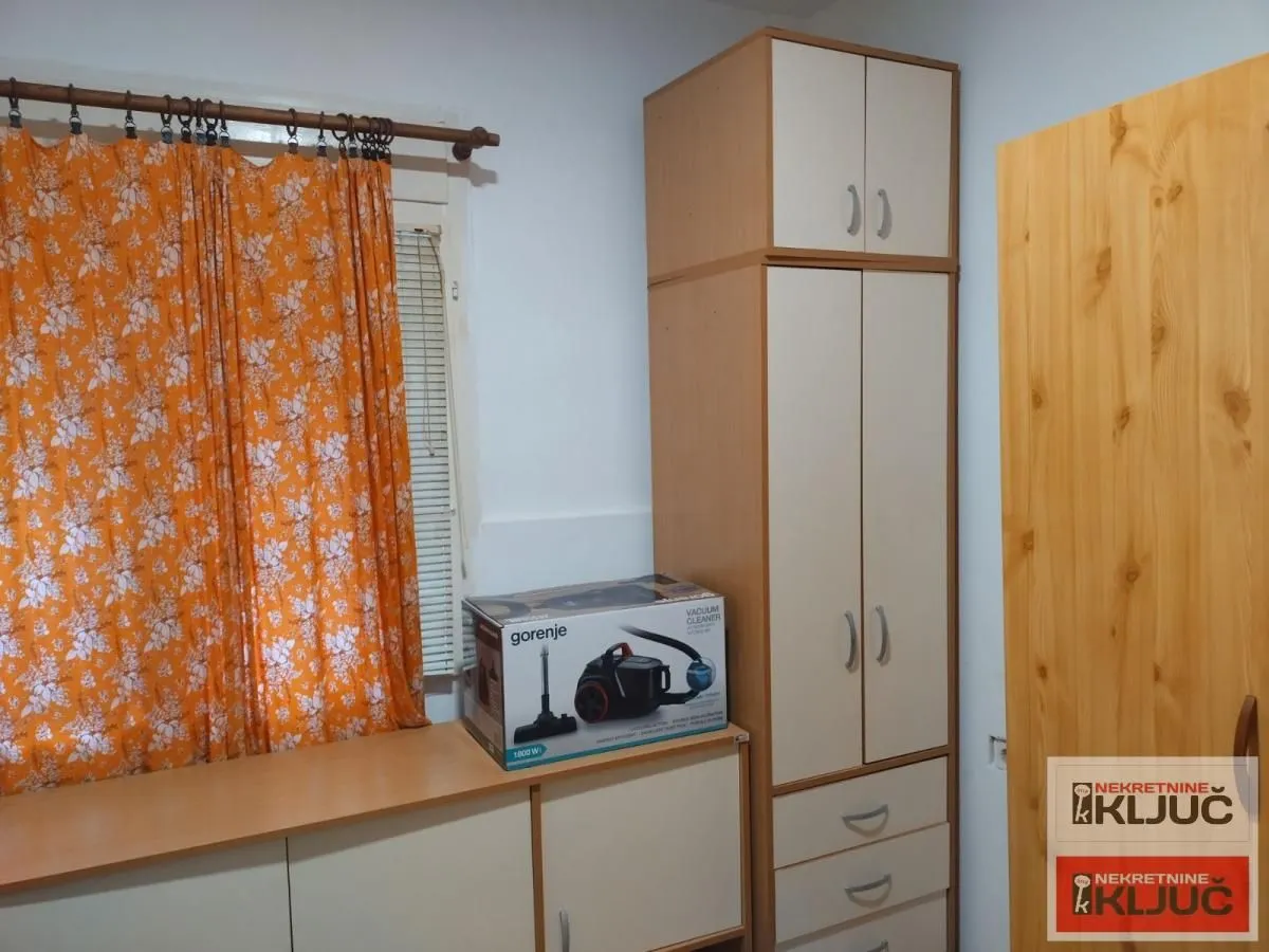Pogled na dio prostorije sa ormarom i narandžastim zavesama.