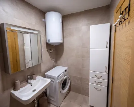 Kupatilo opremljeno umivaonikom, veš mašinom, bojlerom i bijelim ormarićem. - image 5