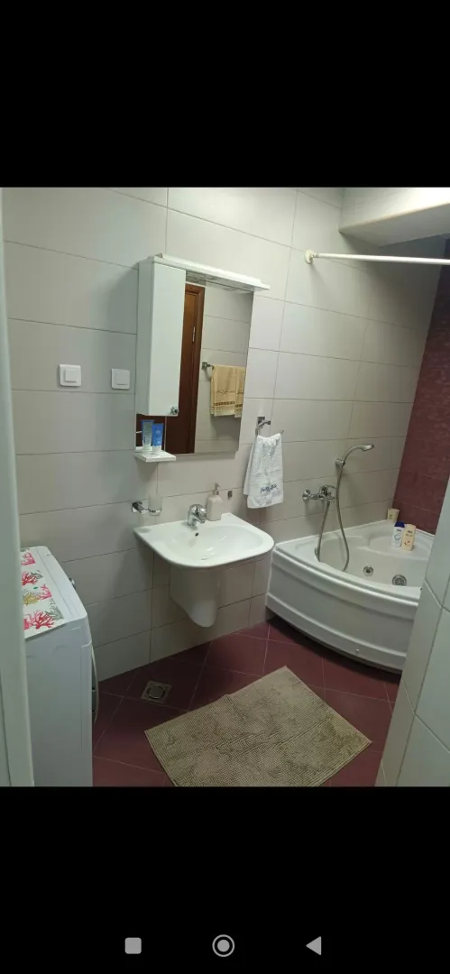 Bathroom equipped with a sink, corner bathtub, and washing machine.