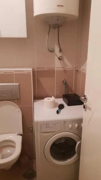 Manje kupatilo sa wc šoljom, veš mašinom i bojlerom na zidu.